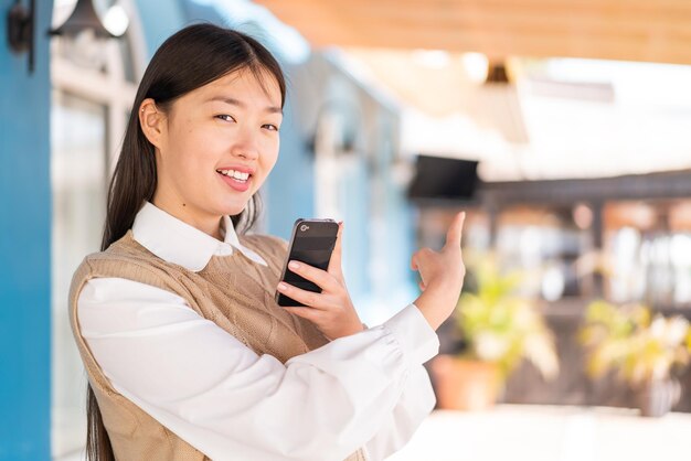 Joven china al aire libre usando un teléfono móvil y apuntando hacia atrás