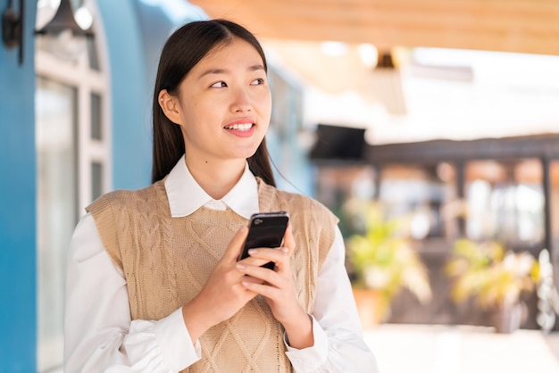 Joven china al aire libre usando teléfono móvil y mirando hacia arriba