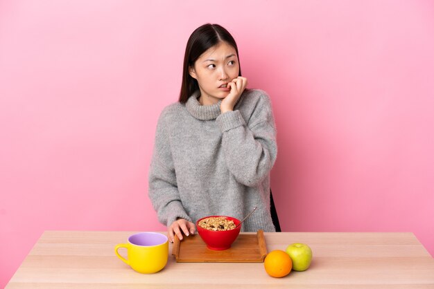 Joven china desayunando en una mesa está un poco nerviosa