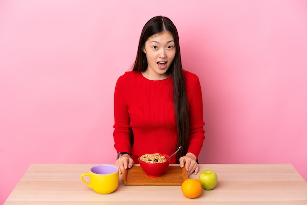 Joven China desayunando en una mesa con expresión facial sorpresa