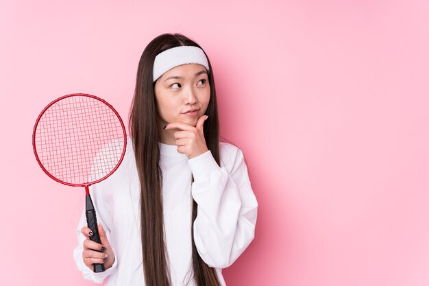 Joven China jugando al bádminton aislado mirando hacia los lados con expresión dudosa y escéptica.