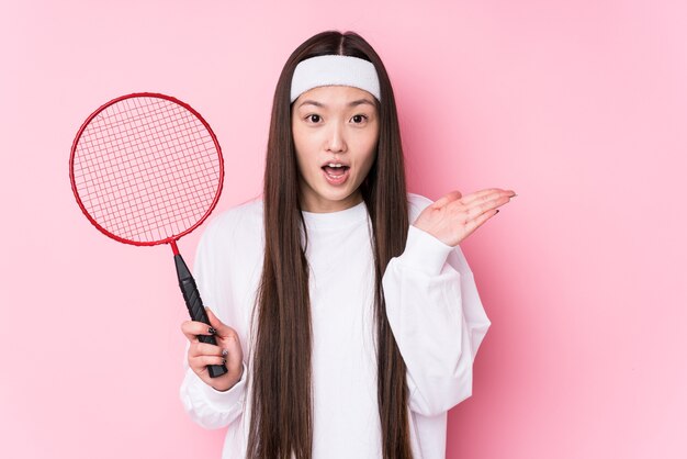 Joven China jugando bádminton aislado sorprendido y conmocionado.