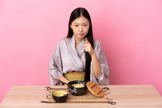 Joven china con kimono y comiendo fideos frustrados y apuntando hacia el frente