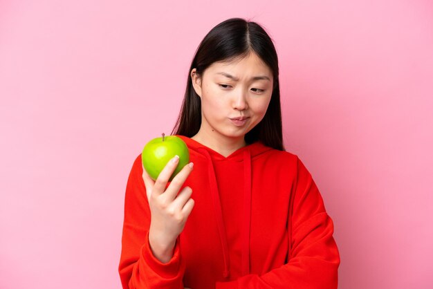 Joven china con una manzana aislada de fondo rosa con expresión triste