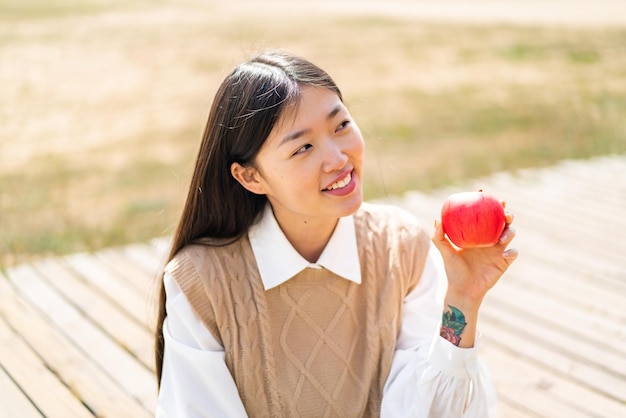 Joven china con una manzana al aire libre mirando hacia arriba mientras sonríe