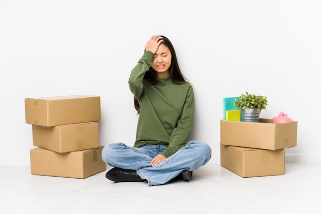 Joven china mudarse a una nueva casa olvidando algo, golpeándose la frente con la palma y cerrando los ojos.