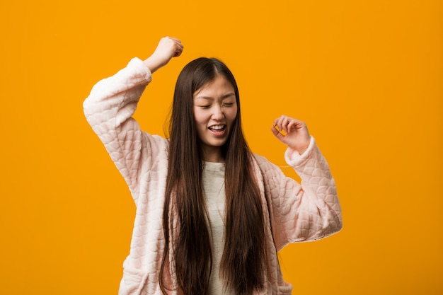 Joven china en pijama celebrando un día especial, salta y levanta los brazos con energía.