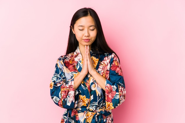 Joven china con un pijama de kimono aislado tomados de la mano en rezar cerca de la boca, se siente seguro.