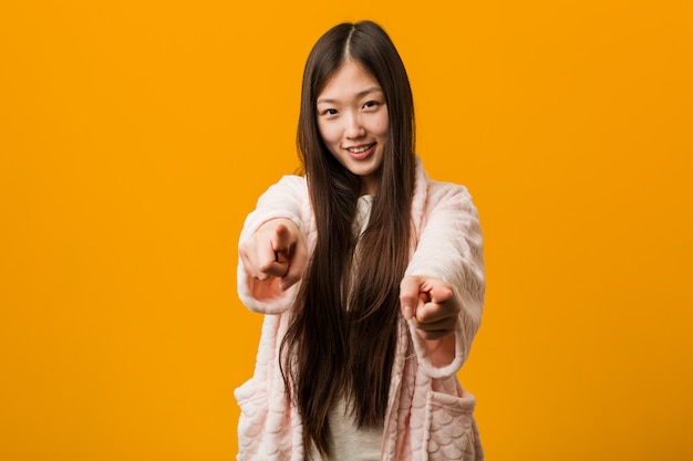 Joven china en pijama sonrisas alegres apuntando al frente.