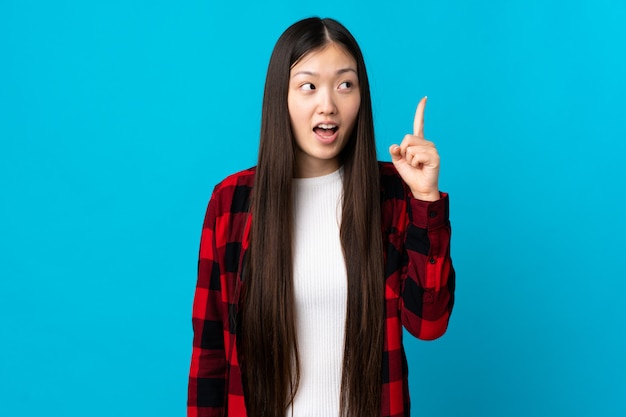 Joven china sobre pared azul aislada con la intención de darse cuenta de la solución mientras levanta un dedo