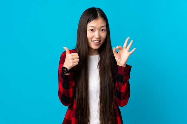 Joven china sobre pared azul aislada mostrando signo bien y pulgar arriba gesto