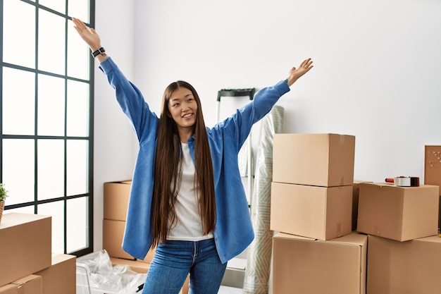 Foto joven china sonriendo feliz y confiada con las manos levantadas en su nuevo hogar