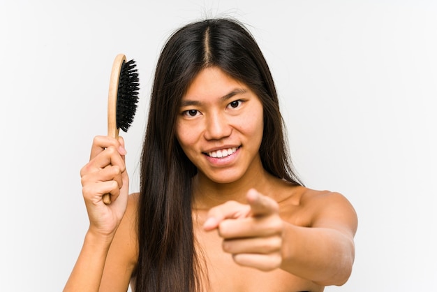 Joven China sosteniendo un cepillo para el cabello aislado alegres sonrisas apuntando al frente.