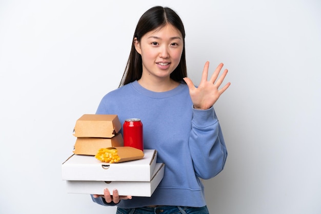 Joven china sosteniendo comida rápida aislada de fondo blanco contando cinco con los dedos