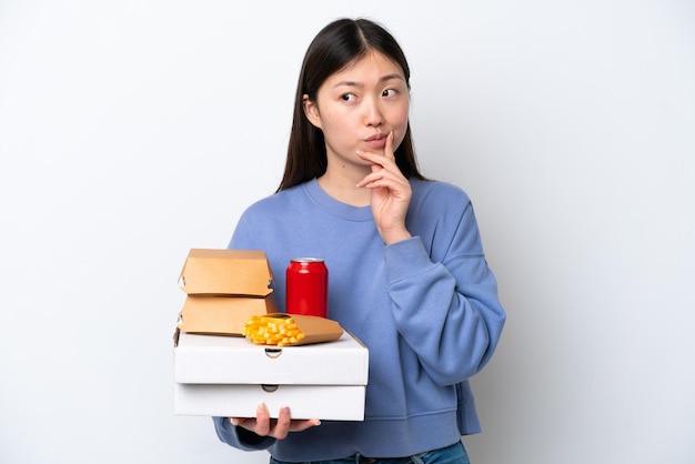 Joven china sosteniendo comida rápida aislada de fondo blanco con dudas y pensando