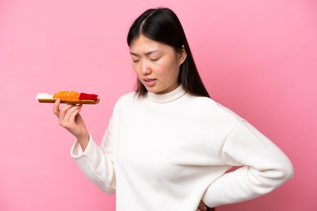 Joven china sosteniendo sashimi aislada de fondo rosado que sufre de dolor de espalda por haber hecho un esfuerzo