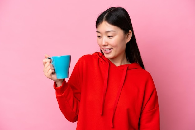 Joven china sosteniendo una taza de café aislada de fondo rosa con expresión feliz