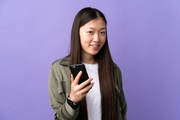 Joven china con teléfono móvil sobre púrpura aislado con expresión feliz