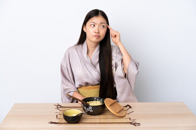 Joven china vestida con kimono y comiendo fideos haciendo el gesto de locura