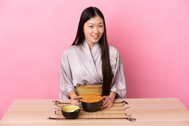 Joven china vistiendo kimono y comiendo fideos en una mesa en rosa