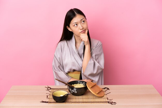 Joven China vistiendo kimono y comiendo fideos teniendo dudas