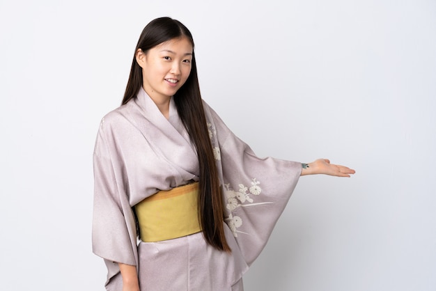 Joven china vistiendo kimono sobre pared aislada extendiendo las manos a un lado para invitar a venir