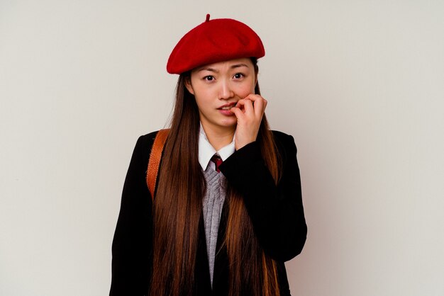 Joven china vistiendo un uniforme escolar aislado sobre fondo blanco mordiéndose las uñas, nerviosa y muy ansiosa.