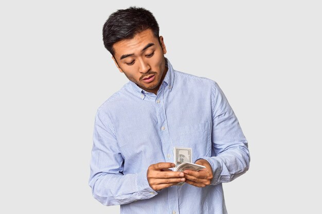 Joven chino contando billetes en efectivo contra el telón de fondo del estudio