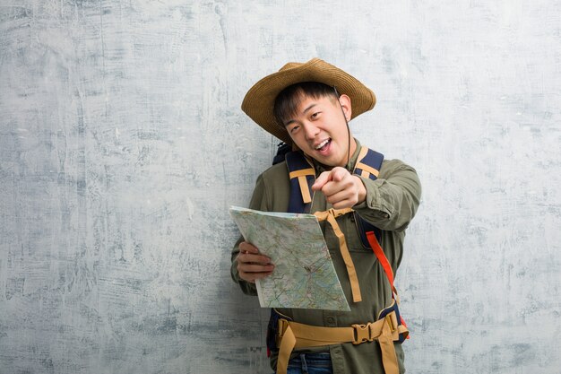 Joven chino explorador hombre sosteniendo un mapa alegre y sonriente apuntando al frente