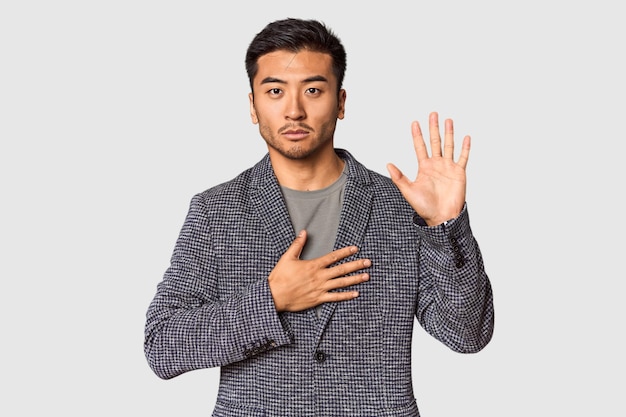 Foto joven chino en el fondo del estudio haciendo un juramento poniendo la mano en el pecho