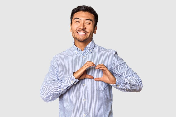 Foto joven chino en el fondo del estudio sonriendo y mostrando una forma de corazón con las manos
