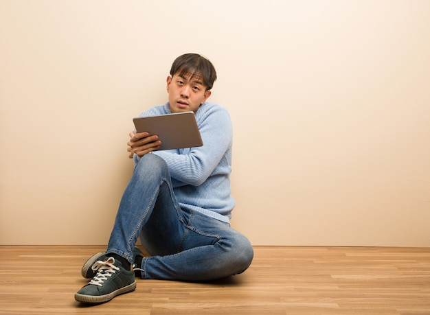 Joven chino sentado usando su tableta enfriándose debido a la baja temperatura