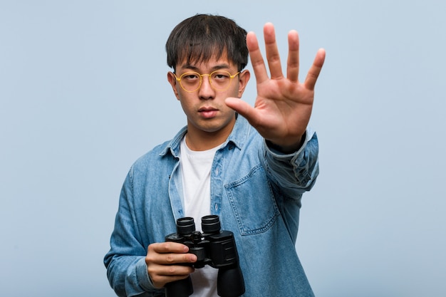 Joven chino sosteniendo un binoculares poniendo la mano delante