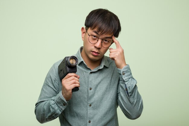 Joven chino sosteniendo una cámara vintage pensando en una idea