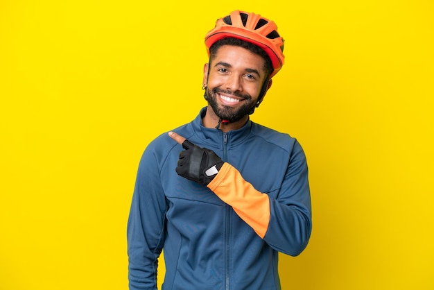 Foto joven ciclista brasileño aislado de fondo amarillo apuntando hacia un lado para presentar un producto