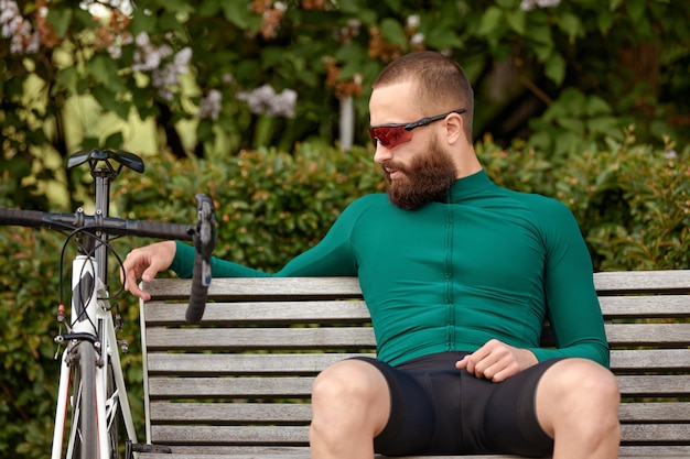 Foto joven ciclista guapo descansa después de un paseo en bicicleta en el parque