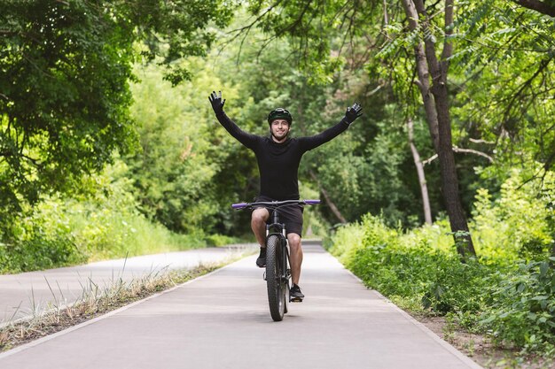 Joven ciclista masculino celebrando la victoria con las manos en alto