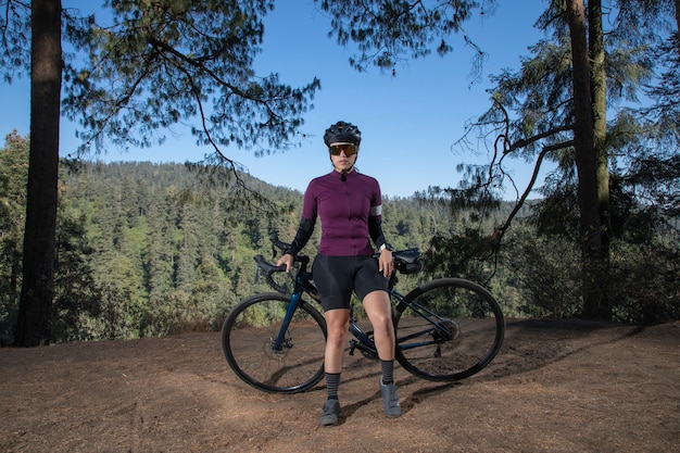 Joven ciclista posando con su bicicleta en un mirador con un paisaje boscoso en el fondo