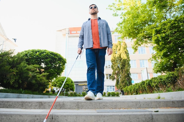 Foto joven ciego con bastón blanco cruzando la calle en la ciudad