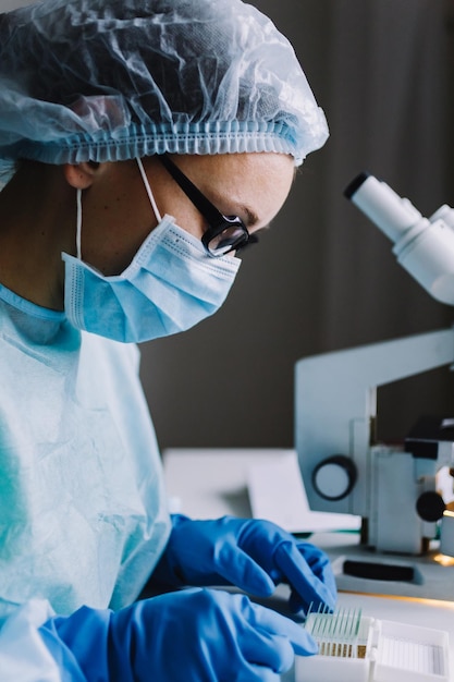 Joven científica en uniforme y máscara arreglando lentes de microscopio en una pequeña caja especial