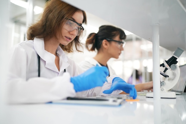 Foto joven científico con bata de laboratorio blanca que trabaja con microscopio binocular en el laboratorio de ciencia de materiales