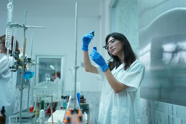 Joven científico con bata de laboratorio blanca que trabaja con microscopio binocular en el laboratorio de ciencia de materiales