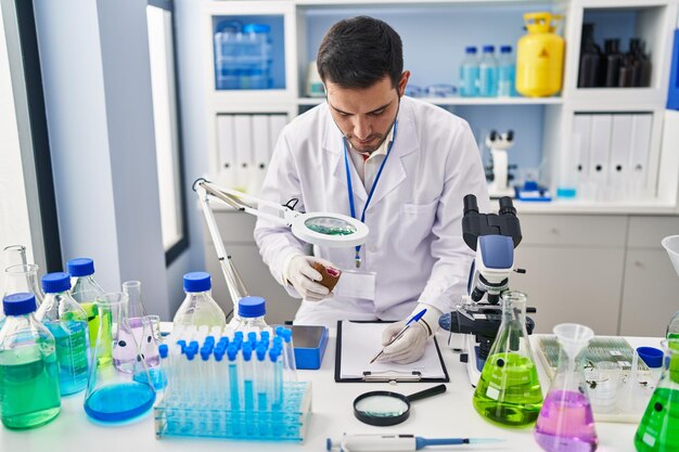Joven científico hispano que sostiene una piedra preciosa escribe en un documento en el laboratorio