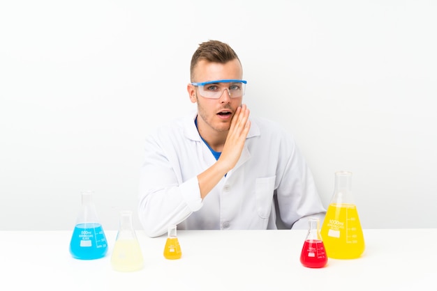 Joven científico con muchos frascos de laboratorio susurrando algo
