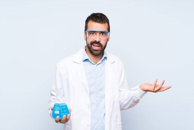 Joven científico sosteniendo frasco de laboratorio sobre pared aislada haciendo gesto de dudas