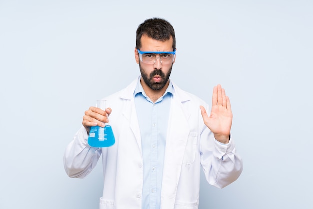 Foto joven científico sosteniendo frasco de laboratorio sobre pared aislada haciendo gesto de parada y decepcionado