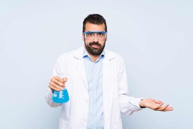 Joven científico sosteniendo frasco de laboratorio sobre pared aislada infeliz por no entender algo