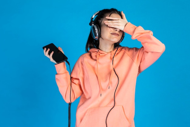 La joven cierra los ojos con la mano y escucha música en los auriculares Foto de alta calidad