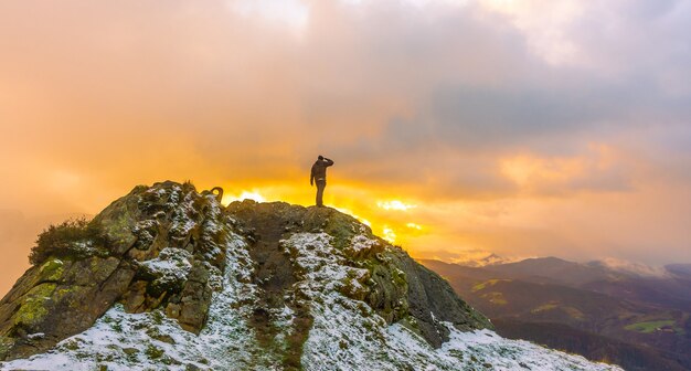 Un joven en la cima de la montaña en el nevado invierno naranja atardecer, en el monte Peñas de Aya en la ciudad de Oiartzun cerca de San Sebastián, España