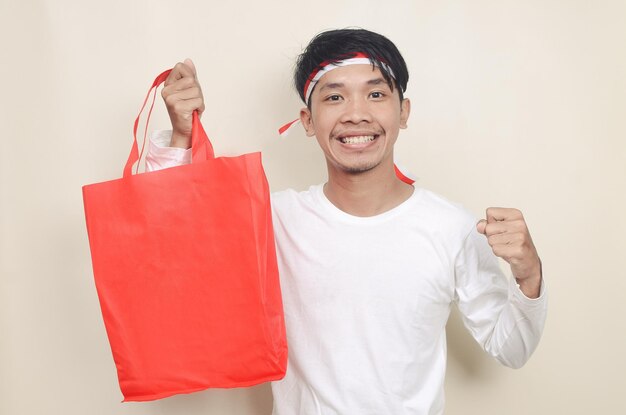 Joven con cinta en la cabeza sosteniendo bolsas de compras en un fondo aislado Concepto de descuento del día de la independencia